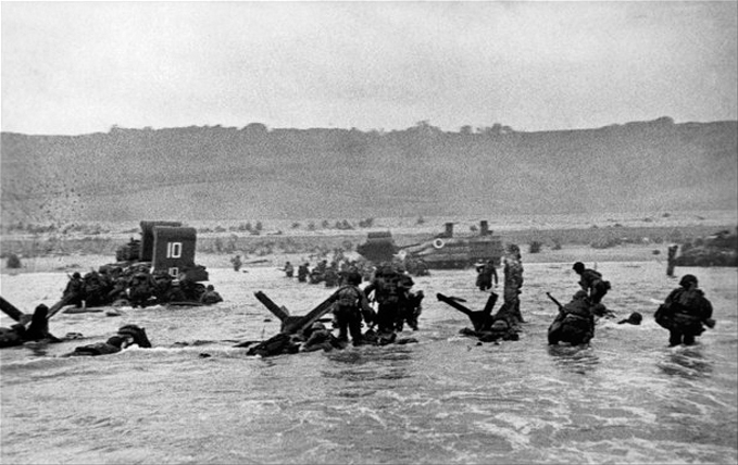 Soldiers wading ashore between obstacles on D-Day